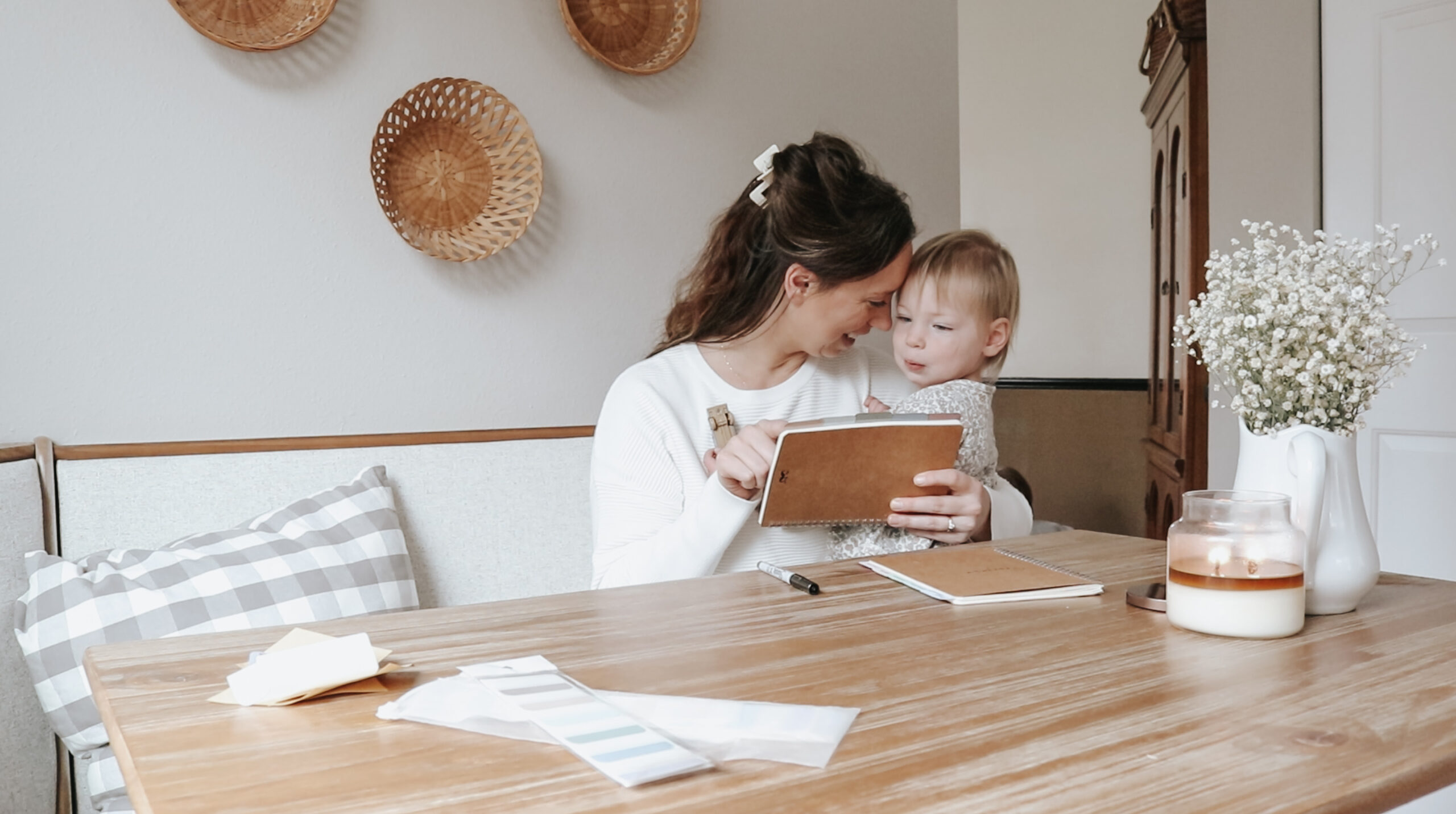 Homemaker snuggles her child while sitting at a table holding her prayer journal